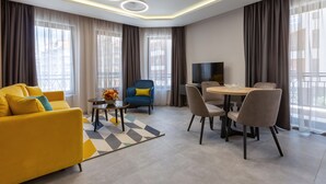 Una sala moderna con un sofá amarillo, un sillón azul, una mesa de comedor con sillas y un televisor.