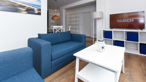 Una sala de estar moderna con un sofá azul, una mesa blanca y un televisor sobre un mueble.