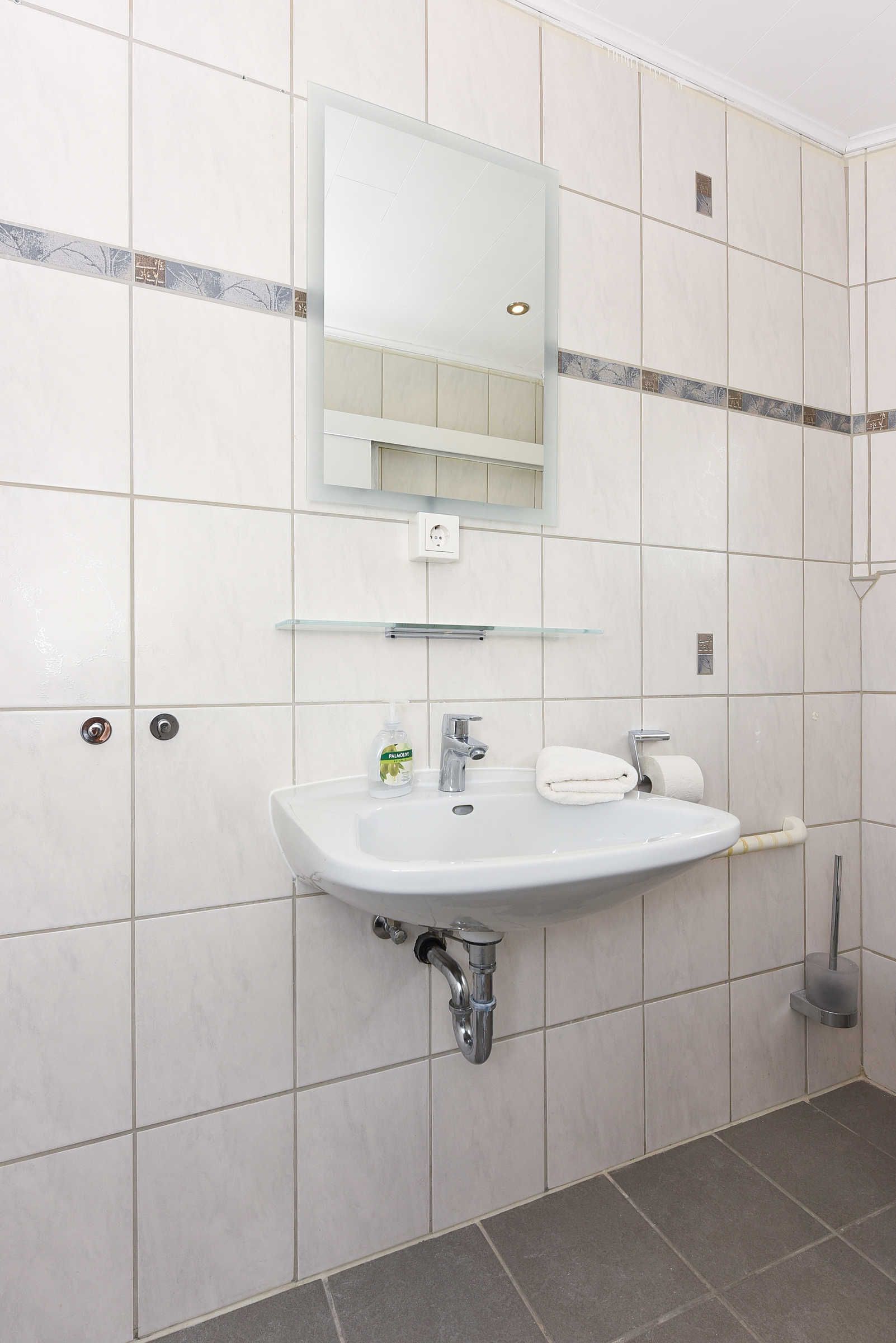 A bathroom with a white sink, mirror, and tiled walls.