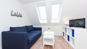 Ein modernes Wohnzimmer mit einem dunkelblauen Sofa, einem weißen Beistelltisch, einem Flachbildfernseher und einer weißen Regaleinheit mit blauen Akzenten.