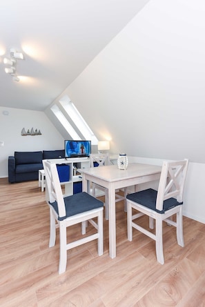 A modern, well-lit room with a dining table, chairs, a TV, and a sofa.