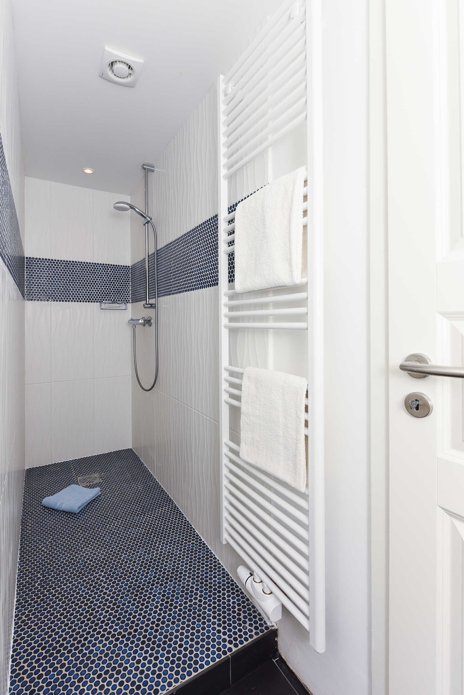 A modern bathroom with a shower, a towel rack, and a radiator.