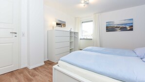 Ein Schlafzimmer mit Bett, Kleiderschrank, einem Fenster mit Vorhängen und einem an der Wand hängenden Kunstwerk.