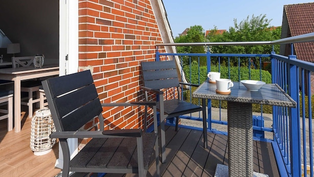 Eine Holzterrasse mit Tisch und Stühlen, einem Korbtablett in der Mitte und einer Backsteinmauer.