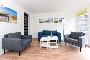 Uma sala de estar moderna com um sofá azul, duas poltronas cinzentas, uma mesa de centro branca e um abajur.