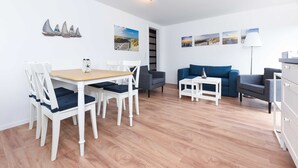 Un soggiorno moderno con zona pranzo, caratterizzato da pavimento in legno, arredi bianchi e decorazioni a tema costiero.