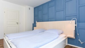 Camera da letto con un letto bianco, una parete d'accento blu e una testiera in legno.