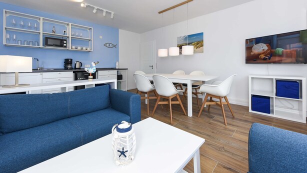 Un soggiorno moderno con un divano blu, un tavolino da caffè bianco e un'area pranzo con un tavolo e sedie bianche.