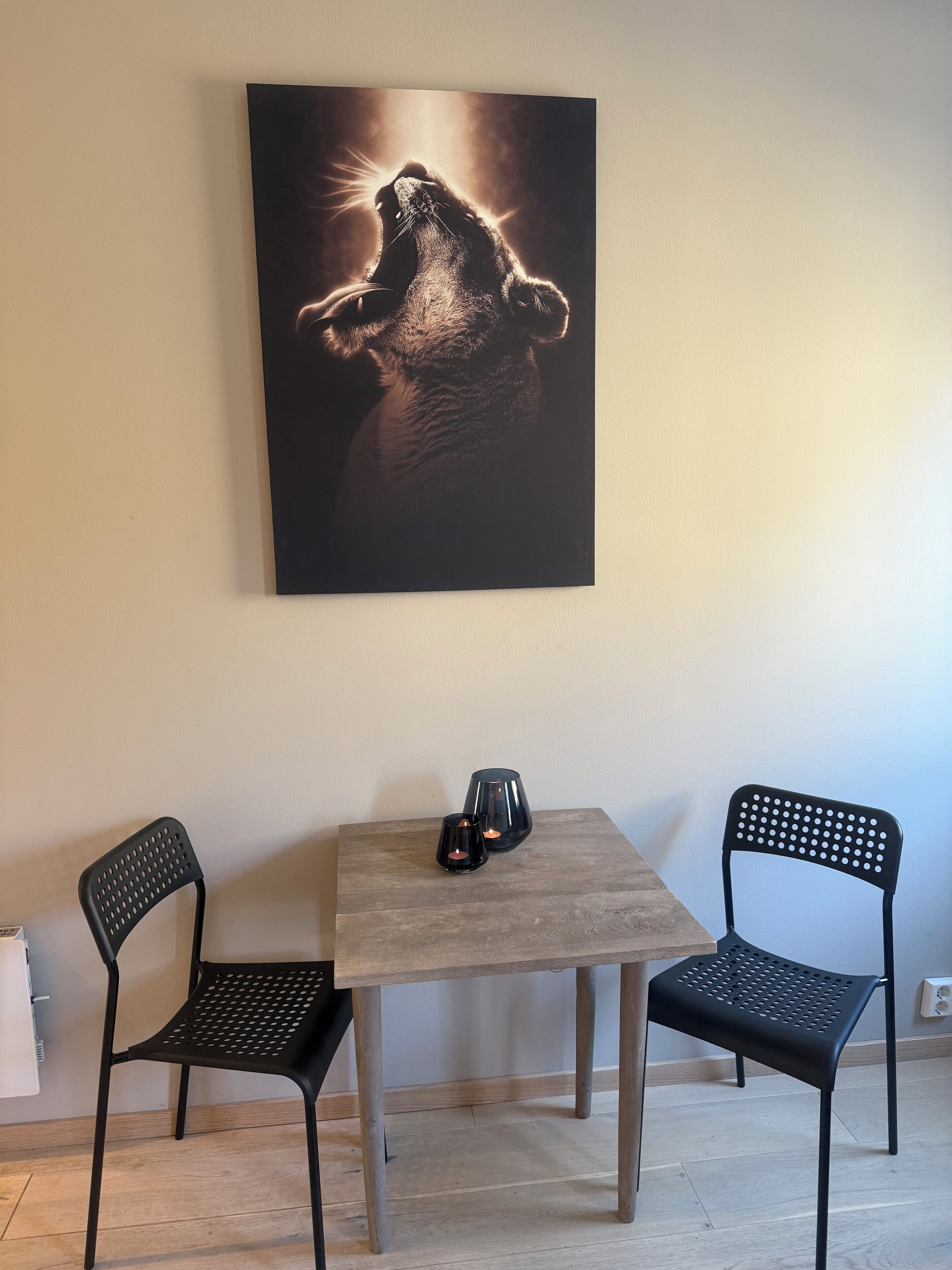 Una habitación con una mesa de madera, dos sillas negras y un cuadro en la pared.