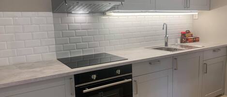 A modern kitchen with a built-in oven, a stainless steel range hood, a double sink, and light gray cabinets.