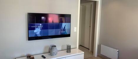 A modern living room with a flat-screen TV mounted on the wall, a white console table with decorative items, and a wooden floor.
