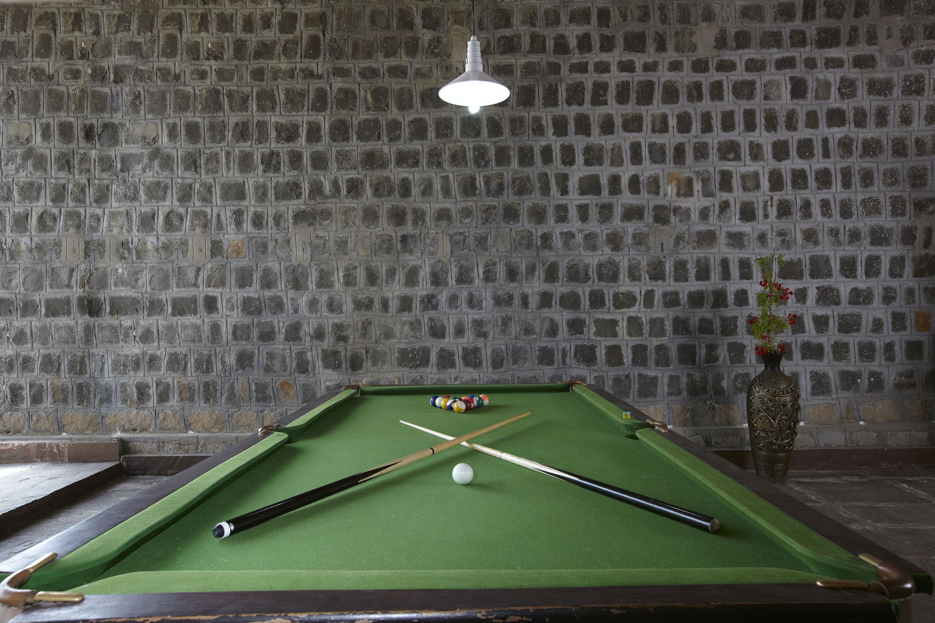 A pool table with a green felt surface, a white cue ball, and two pool cues. There is a vase with flowers on the right side of the table.
