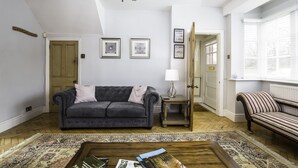 A living room with a dark grey sofa, a patterned rug, a wooden coffee table, and a chandelier. - The cottage is a short walk to the Station, with trains to Liverpool / chester,  (Wirral, Merseyside)