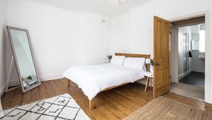 A bedroom with a wooden bed, a large mirror, a white door, and a small bedside table. - The cottage is a short walk to the Station, with trains to Liverpool / chester,  (Wirral, Merseyside)