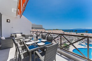 Eine Dachterrasse mit Esstisch, Stühlen und Blick auf Pool und Strand.