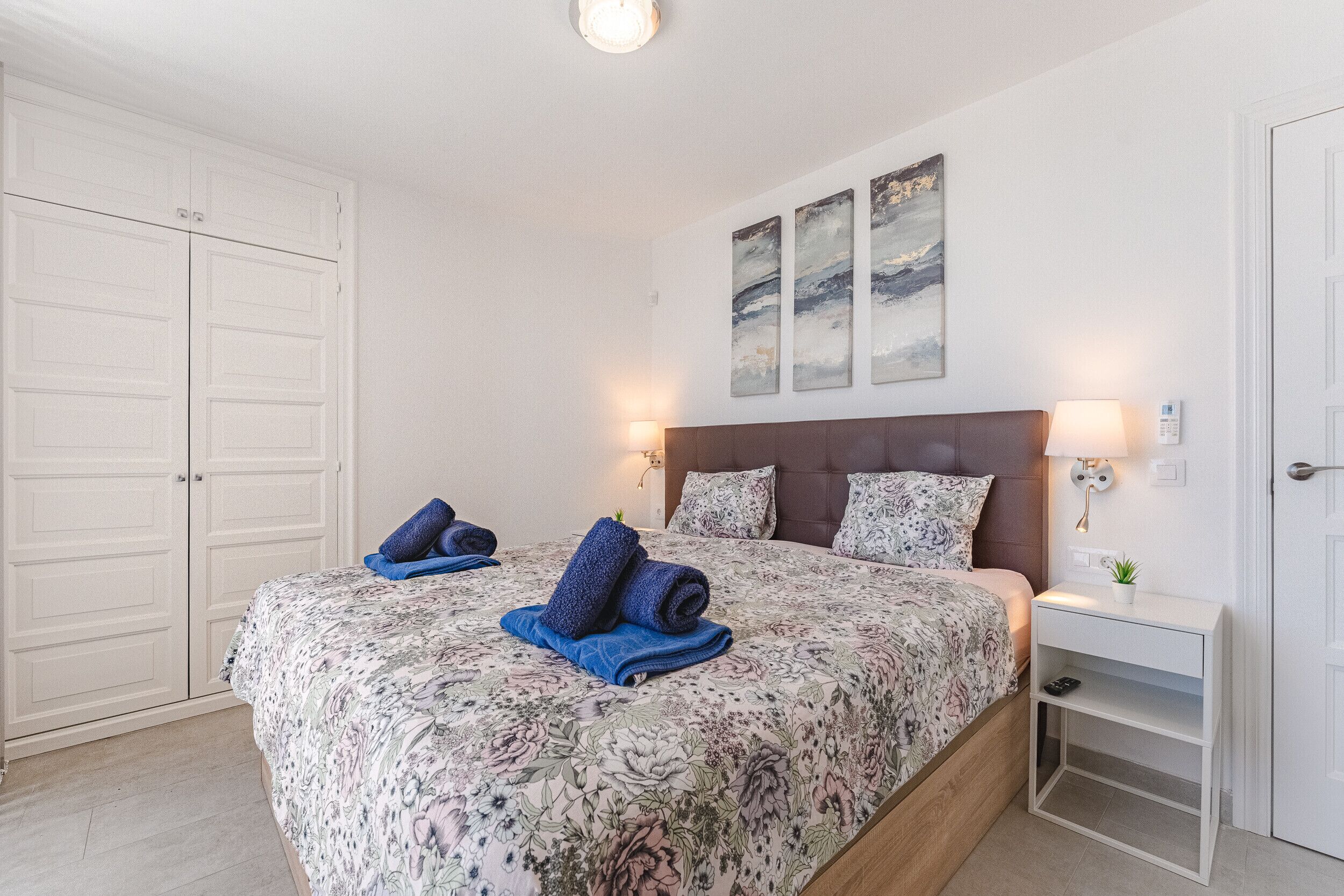 Een slaapkamer met een bed, nachtkastje, wandlamp en een deur.