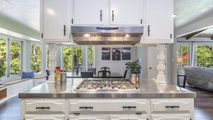 Cozinha com armários brancos, fogão de aço inoxidável e área de refeições com mesa e cadeiras.