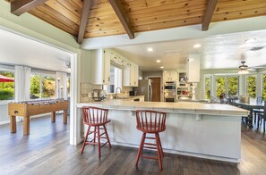 A spacious kitchen with a large island, wooden ceiling beams, and a view of the outdoors. - Starry Pines- BBQ/spa/affordable (Oakhurst)