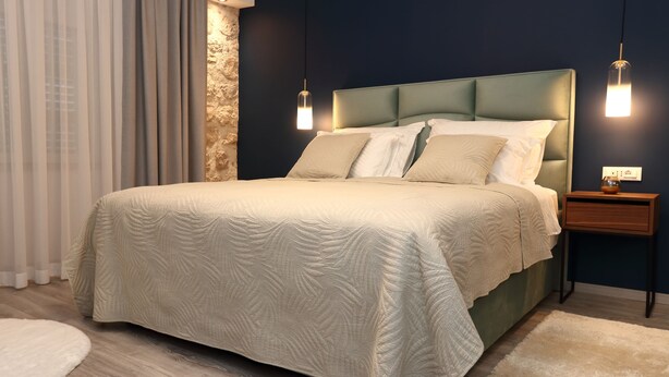 A neatly made bed with a quilted headboard, a bedside table with a vase, and a wall-mounted light fixture.