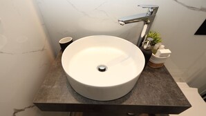 A bathroom with a white sink, a black cup, and a small plant on the counter.