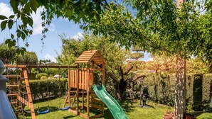 A wooden play structure with a slide and swings in a garden. - Casa el Altico, Lujosa Casa Rural con Unas Vistas Increíbles en Plena Naturaleza (Cehegín)