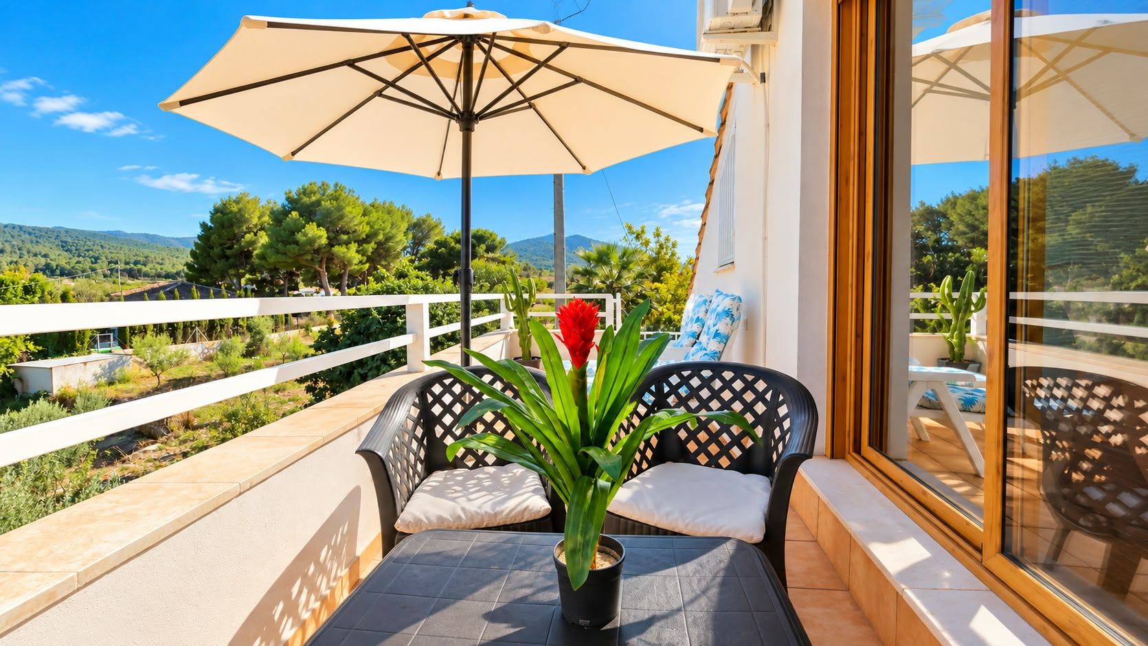 A balcony with a table, two chairs, a potted plant, and a large umbrella.