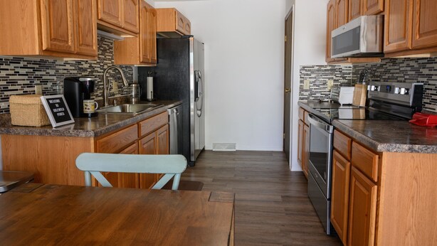 A kitchen with wooden cabinets, a stainless steel refrigerator, a microwave, and a sink. There is a bench and a toaster on the counter.