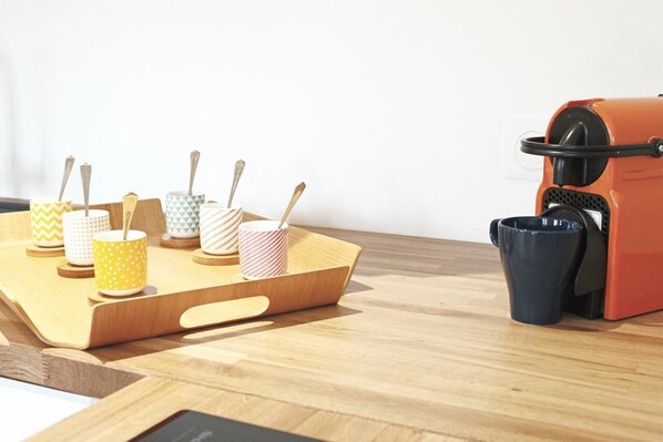 A kitchen area with a coffee machine, a tray with various mugs, and a wooden table.