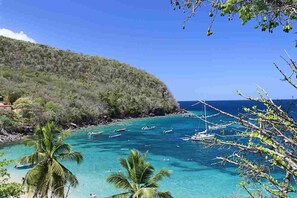 A coastal view with clear turquoise waters, boats, and a mountainous backdrop.