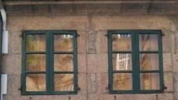 Un edificio de dos pisos con una puerta verde, dos ventanas con contraventanas verdes y un balcón pequeño.