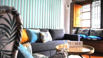 Una sala de estar acogedora con un sofá gris, cojines estampados, una mesita redonda de madera con una vela, y un letrero que dice 'HOME'.