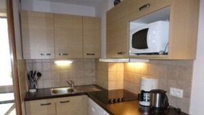 Cozinha compacta com armários de madeira, pia de aço inoxidável e cafeteira no balcão.