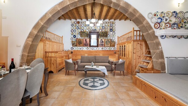 A cozy living room with a stone arch, wooden furniture, a dining area, and a wall decorated with plates.