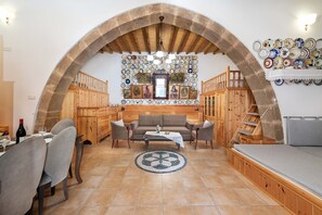 A cozy living room with a stone arch, wooden furniture, a dining area, and a wall decorated with plates. - Traditional House Leventis (Archangelos)