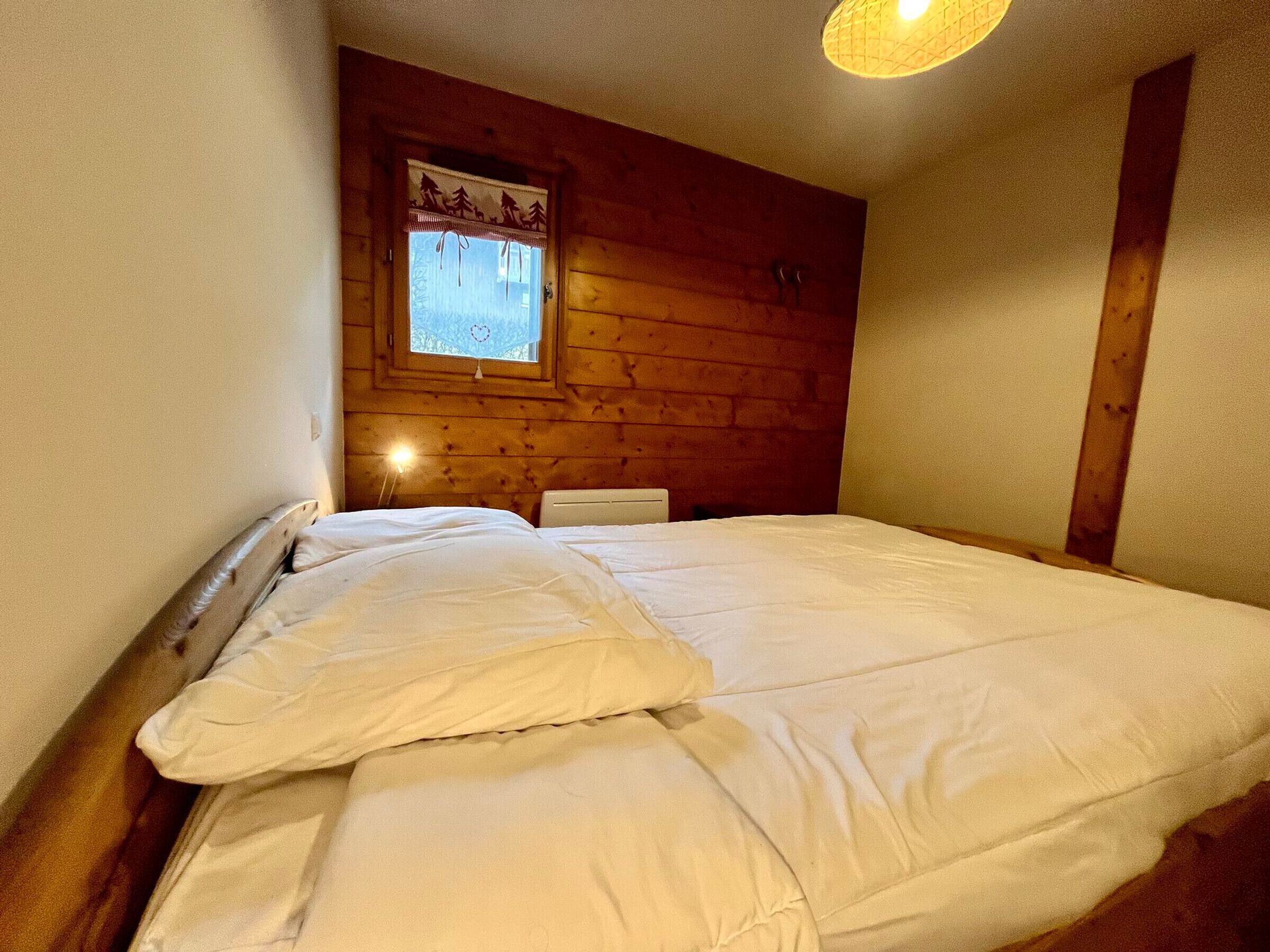 A single bed in a room with wooden walls and a window with a curtain.