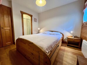 A bedroom with a wooden bed, a nightstand with a lamp, a wooden wardrobe, and a shower area. - T3 Apartment in Samoëns center with terrace and garage (Samoëns)