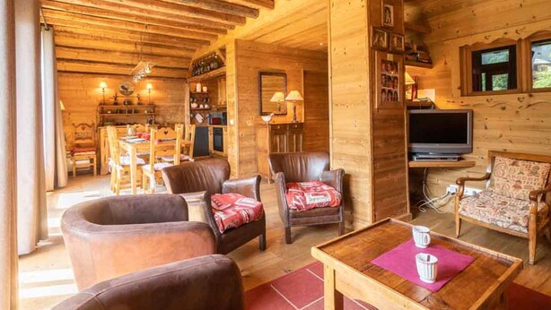 Ein gemütliches Holzhaus-Interieur mit Essbereich, Wohnzimmer mit Ledersofas, Fernseher und Kamin.