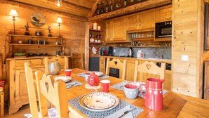Ein Holzhütten-Interieur mit einem Esstisch für vier Personen, Holzschränken und einer Küchenzeile mit Geräten.