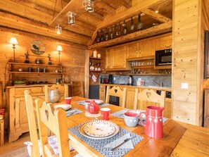 Puinen mökki, jonka sisätiloissa on ruokapöytä neljälle, puiset kaapit ja keittiö, jossa on kodinkoneet.