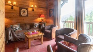 Ein gemütliches Holzhaus-Interieur mit einer Couch, zwei Sesseln, einem kleinen Tisch und einem Fenster mit Bergblick.