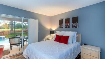A bedroom with a large bed, a nightstand, a lamp, and a view of a patio with chairs and a table.
