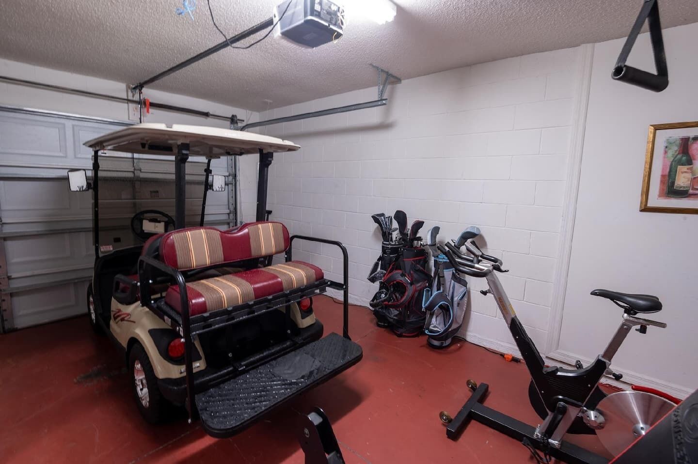 A compact garage with a golf cart, a stationary exercise bike, and a wall-mounted bicycle.