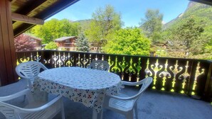 A covered outdoor seating area with a table and chairs, overlooking a mountainous landscape.
