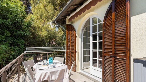 An outdoor patio with a table set for dining, surrounded by a wooden fence and trees. - GuestHost - Cozy 70 sqm apartment with terrace, able to accommodate up to 6 people, located on the 1st floor of a renovated villa (NO lift) 200 meters from the beach. The property boasts a shared garden and a private parking space. The accommodation, sur (Sanremo)