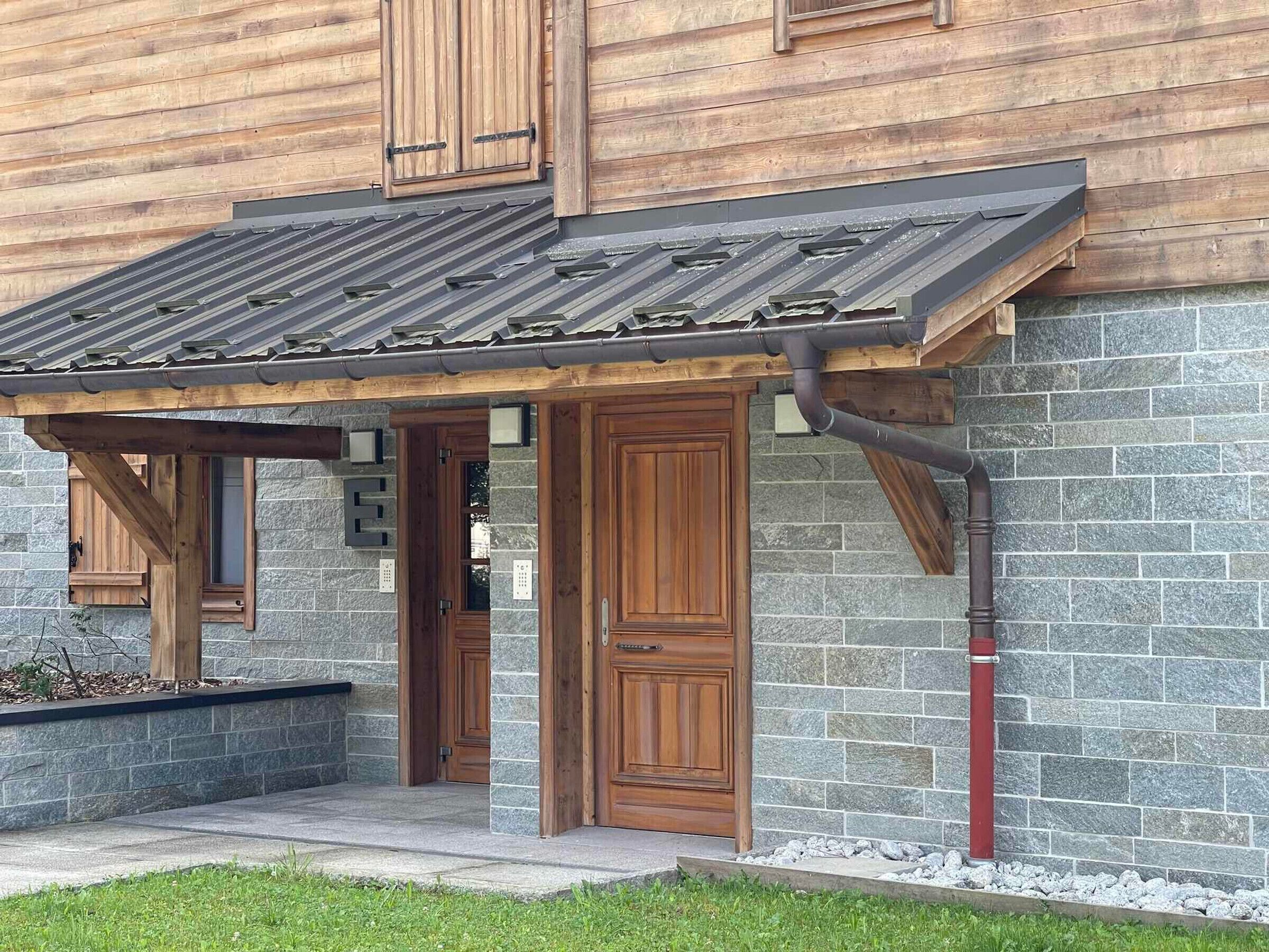 Un bâtiment en bois doté d’une façade en pierre, d’un porche et d’un toit en métal.