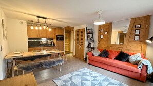 Een moderne woonkamer met een houten bank, een eettafel en een keuken met houten kastjes en een ingebouwde oven.