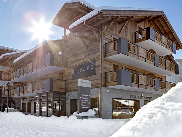 A multi-story building with a wooden facade and balconies, labeled "Alexane." It includes a restaurant and spa facilities.