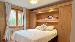 Een gezellige slaapkamer met een houten bed, een raam met gordijnen en ingebouwde planken boven het bed.