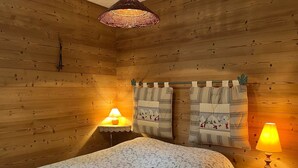 Une pièce de style cabane en bois, comprenant un lit, deux tables de chevet avec lampes et un luminaire suspendu au plafond, fait de fibres tressées.