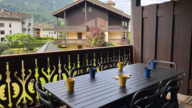 Un balcon avec une table et des chaises, donnant sur une montagne et des immeubles d’habitation.